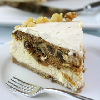 Slice of carrot cake cheesecake on a white plate with a fork. Rest of cheesecake in background.