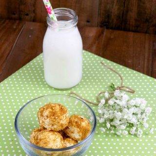 Key lime cheesecake bites in a small glass bowl. Glass jug of milk with straw in background.