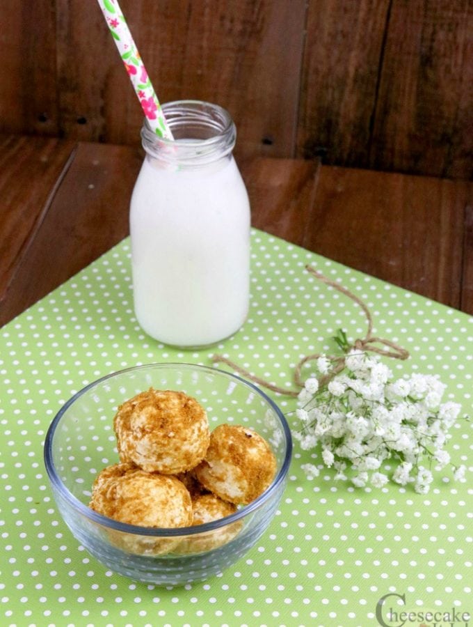 Key lime cheesecake bites in a small glass bowl. Glass jug of milk with straw in background.