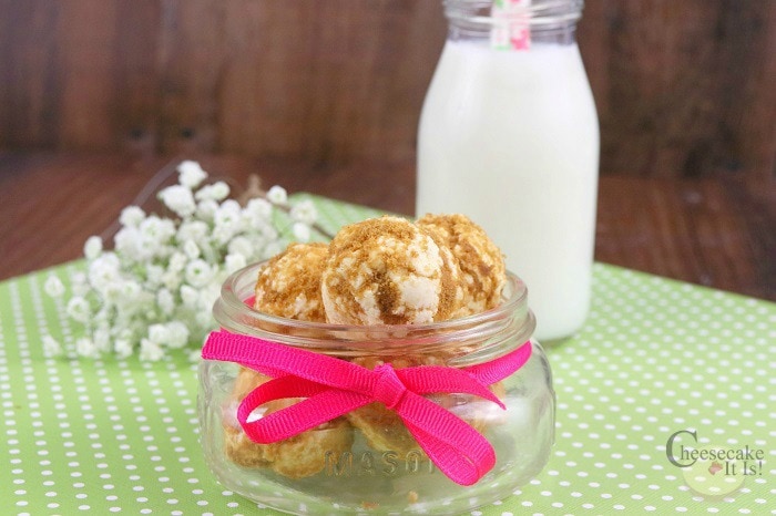 Key lime cheesecake bites in a small glass jar with pink bow. Glass jug of milk with straw in background.