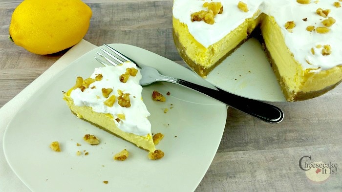 To the right is the whole cheesecake with a slice cut out. To the left a slice of lemon lush cheesecake on a white plate with a fork.