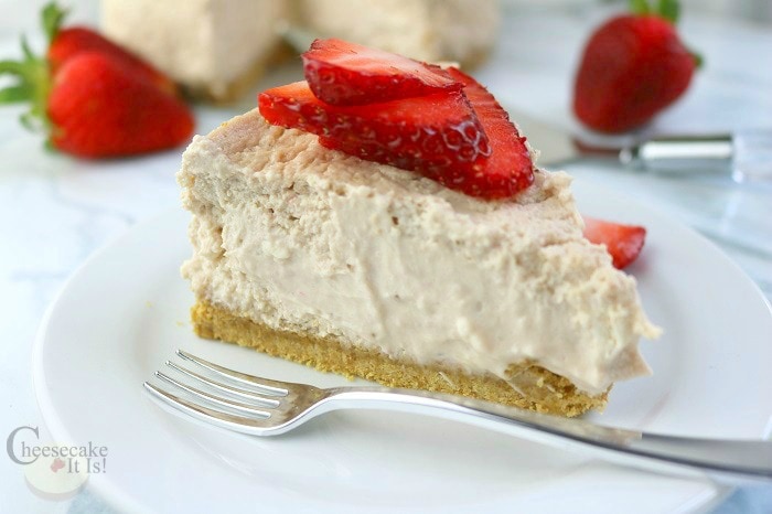 Side view of a slice of Strawberry cheesecake on a white plate with a fork.