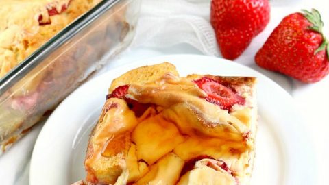 Slices of Strawberry Cheesecake French Toast Bake on white plate with syrup. Rest in background with syrup jar.