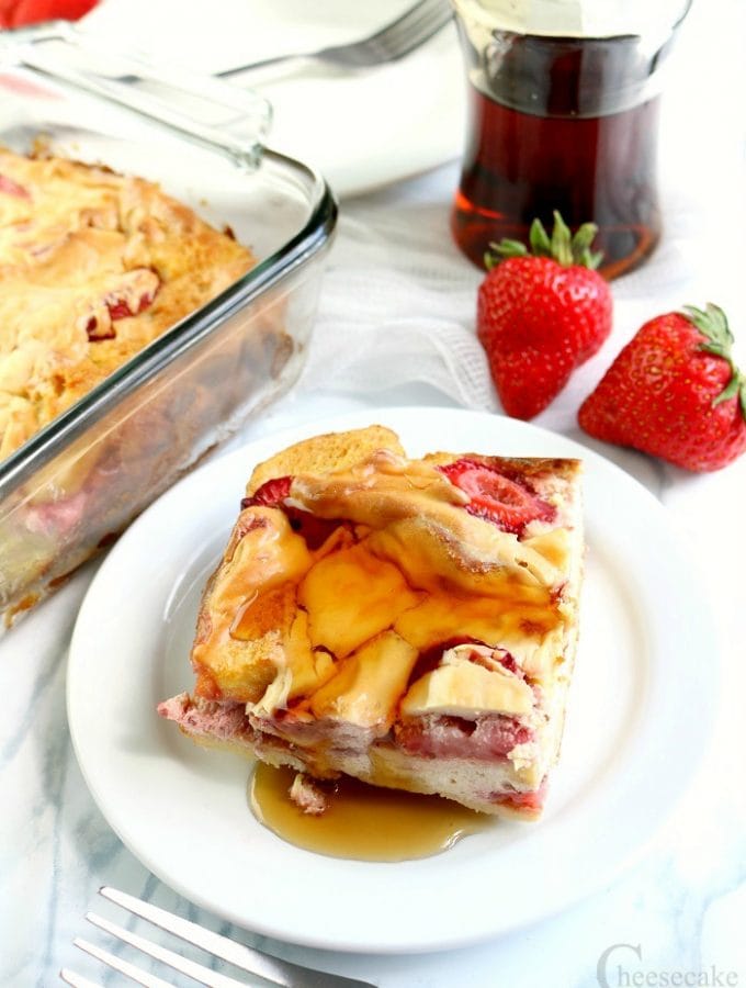 Slices of Strawberry Cheesecake French Toast Bake on white plate with syrup. Rest in background with syrup jar.