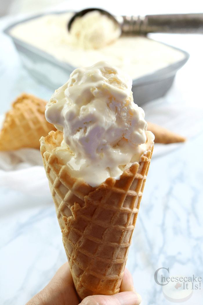 Hand holding a ice cream cone full of cheesecake pineapple ice cream.