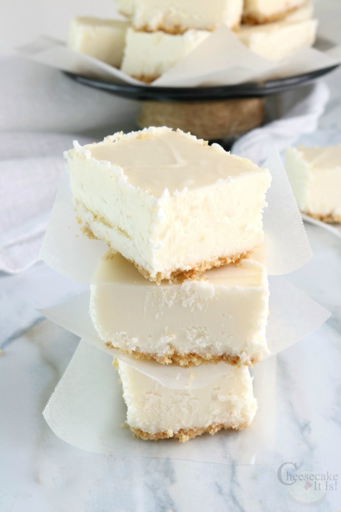 Stack of 3 pieces of cheesecake fudge with plate of more fudge in back.