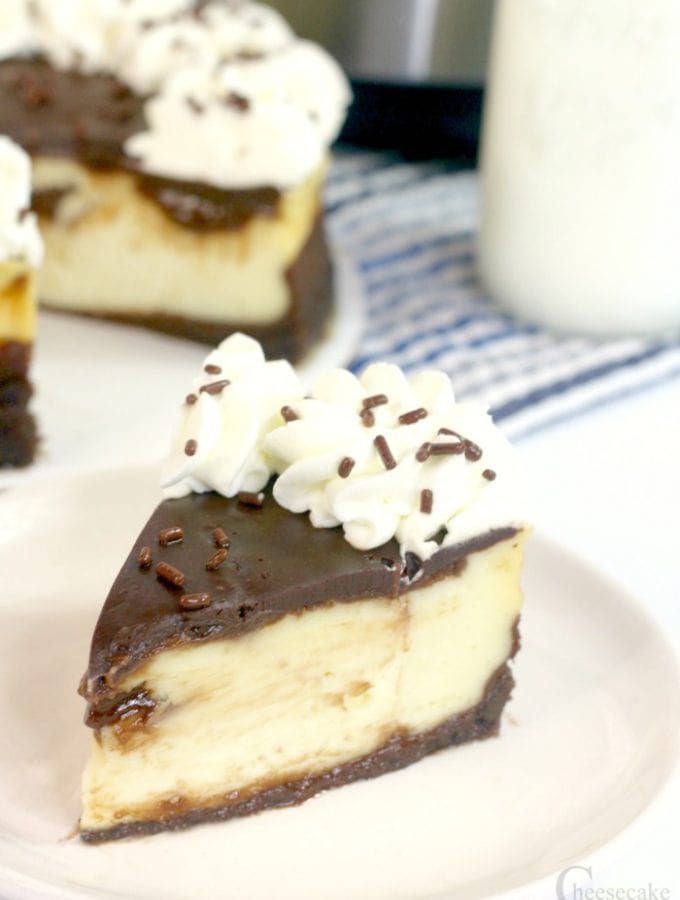 Slice of brownie bottom cheesecake on white plate with rest of cheesecake and Instant Pot in background.