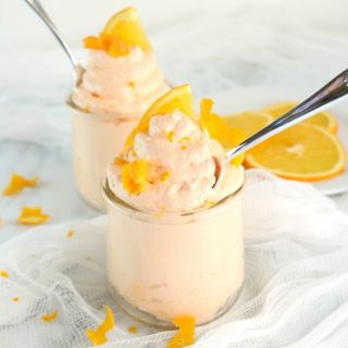 Two small glass jars full of keto orange cheesecake mousse with spoons in them.