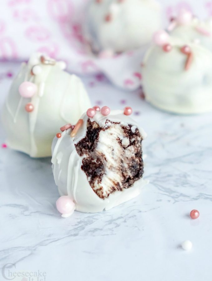 Oreo cheesecake bites with one having a bite missing so you see the inside.