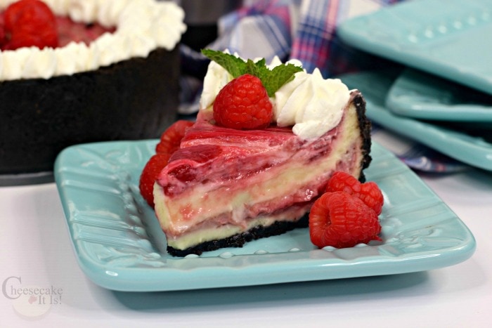 Slice of raspberry cheesecake on blue plate with fresh raspberries