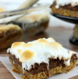 Baked S'mores cheesecake bar on wax paper with pan of bars in background