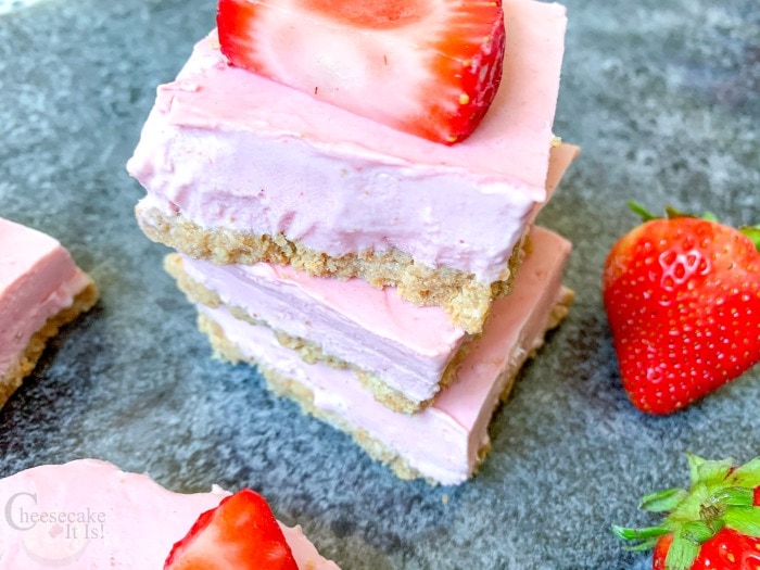 3 Cheesecake bars stacked on top of each other with fresh strawberries on the side