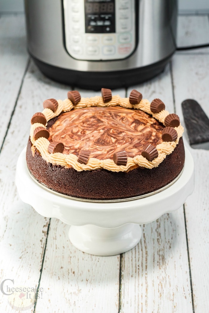 Chocolate Peanut Butter Cheesecake on white cake stand with Instant Pot in background