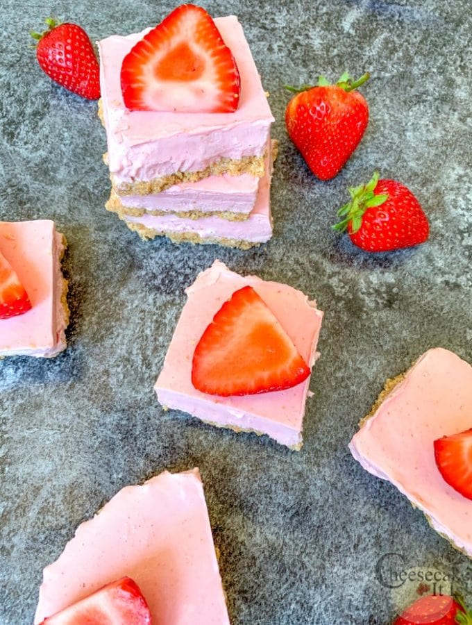 Strawberry cheesecake bars on stone counter with fresh strawberries on top