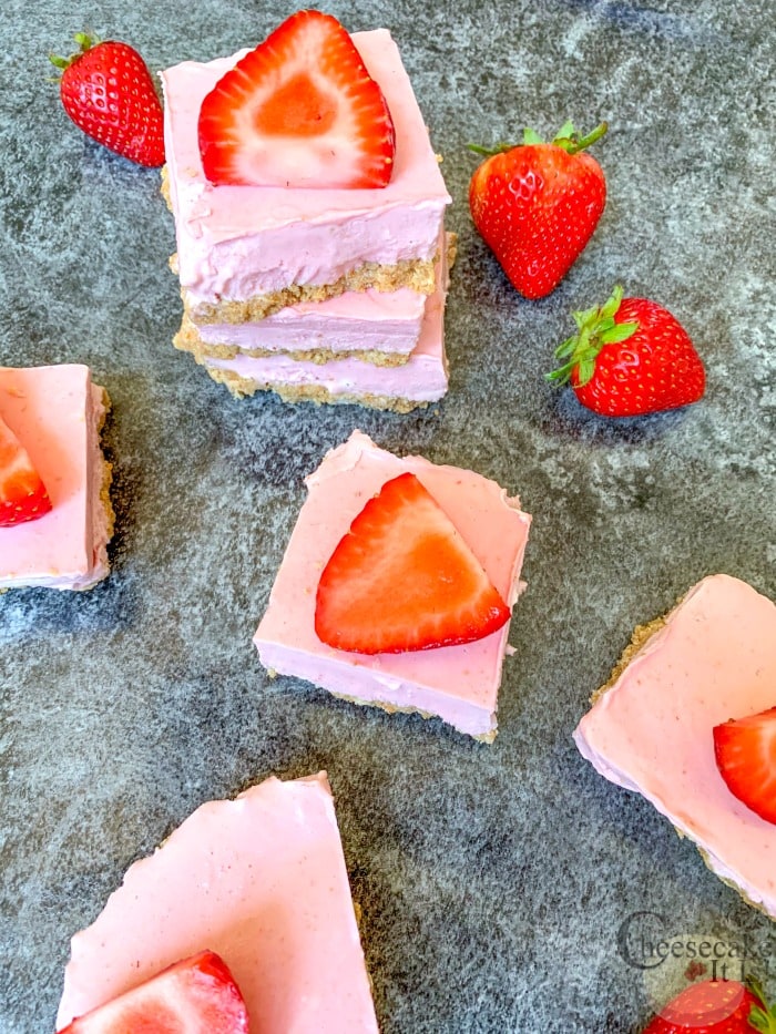 Strawberry cheesecake bars on stone counter with fresh strawberries on top