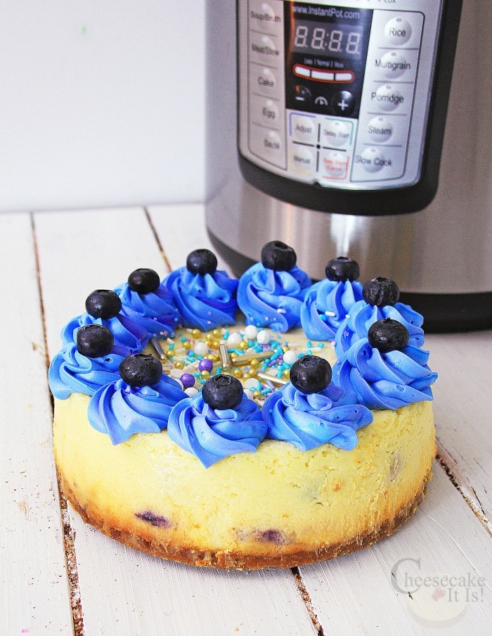 Whole cheesecake with blue frosting and fresh blueberries on top