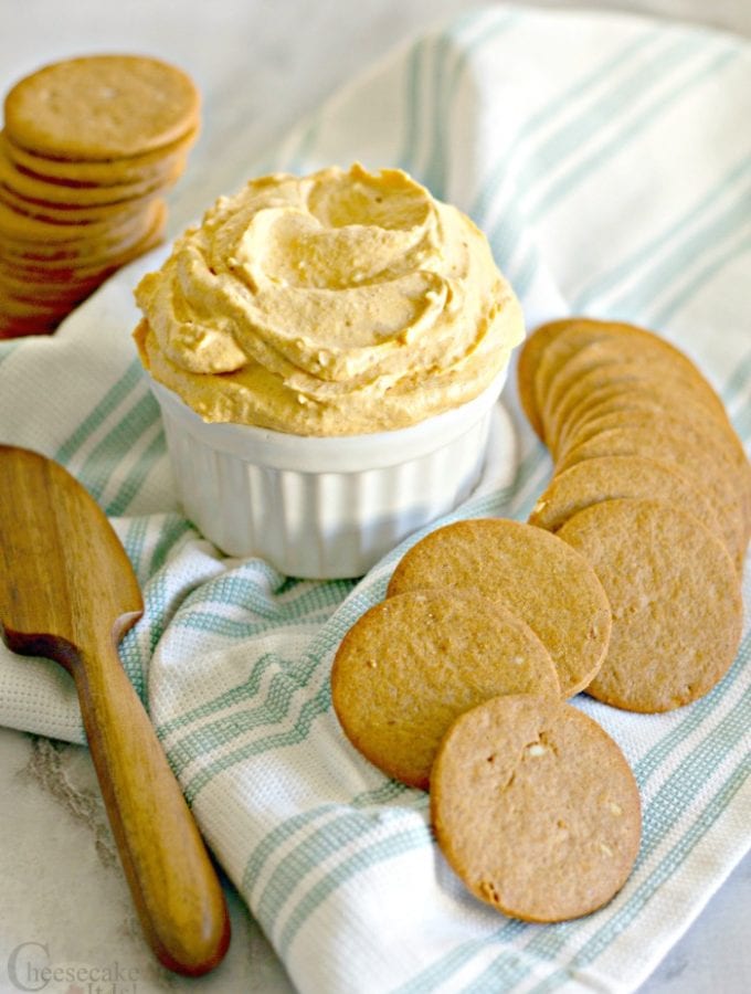 White bowl full of pumpkin cheesecake dip with cookies around it.
