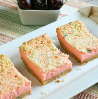 3 cheery cheesecake bars on white plate with whole cherries in background