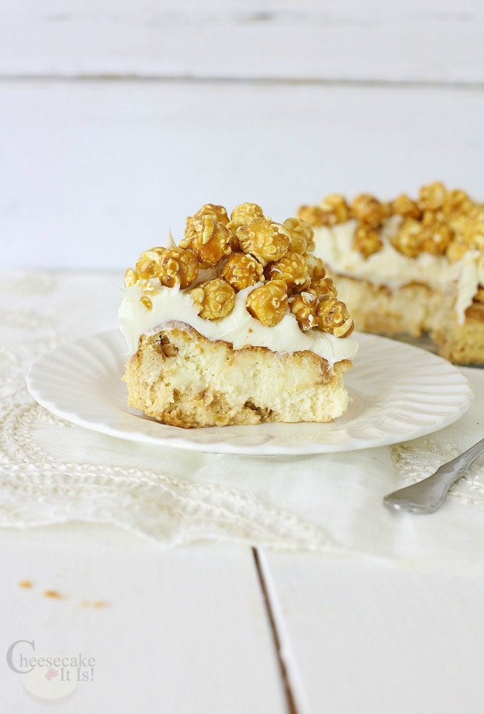 Slice of caramel popcorn cheesecake on white plate with rest of cheesecake in background