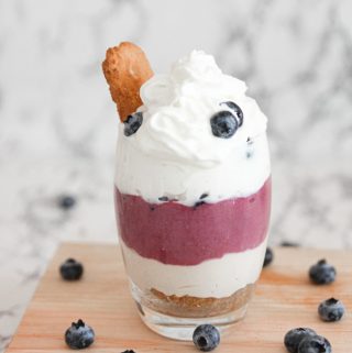 Finished no bake blueberry cheesecake in a glass topped with whipped topping and fresh blueberries
