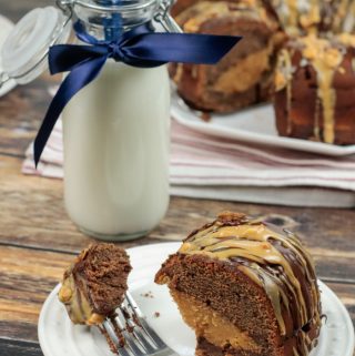 Slice of Peanut Butter Cheesecake Filled Chocolate Bundt Cake on white plate with rest of cake in background with a bottle of milk
