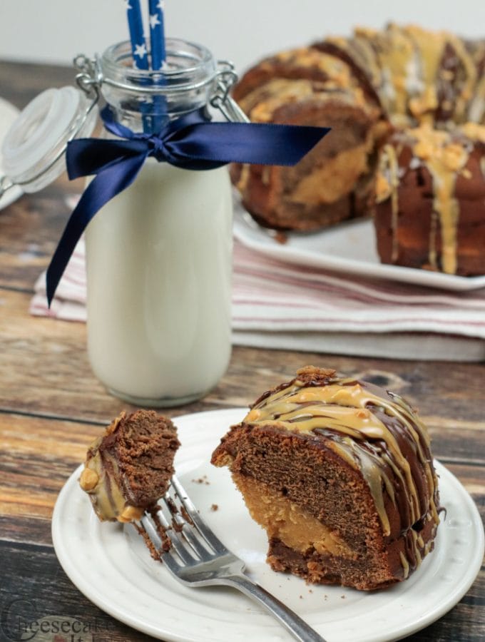 Slice of Peanut Butter Cheesecake Filled Chocolate Bundt Cake on white plate with rest of cake in background with a bottle of milk