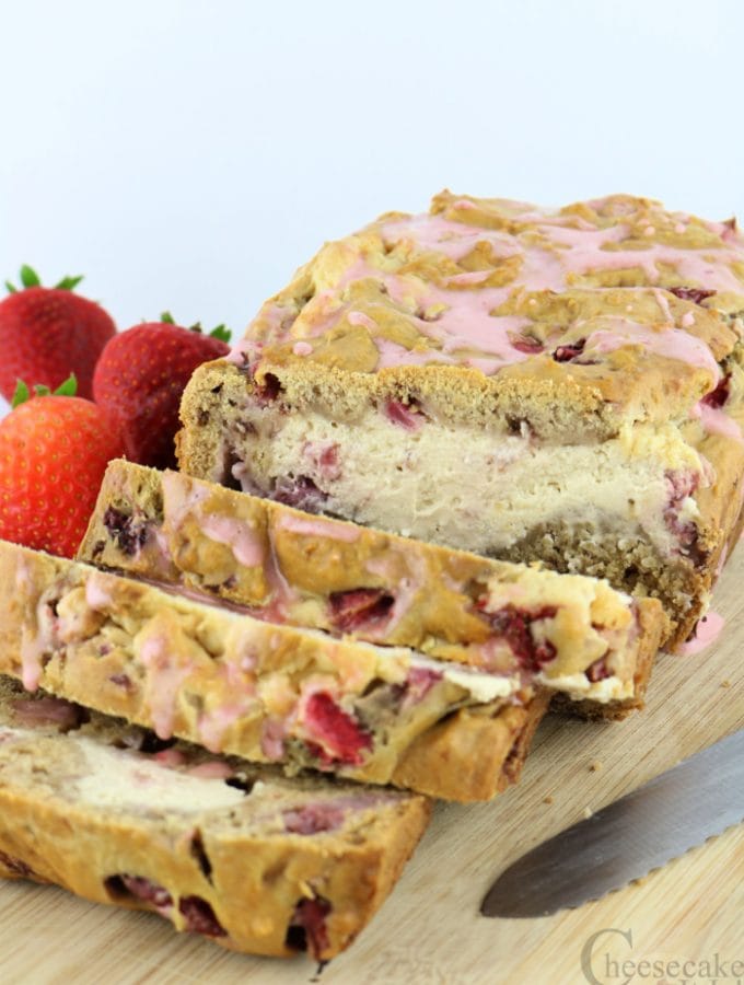 Sliced strawberry cheesecake bread on wood cutting board with fresh strawberries to the side