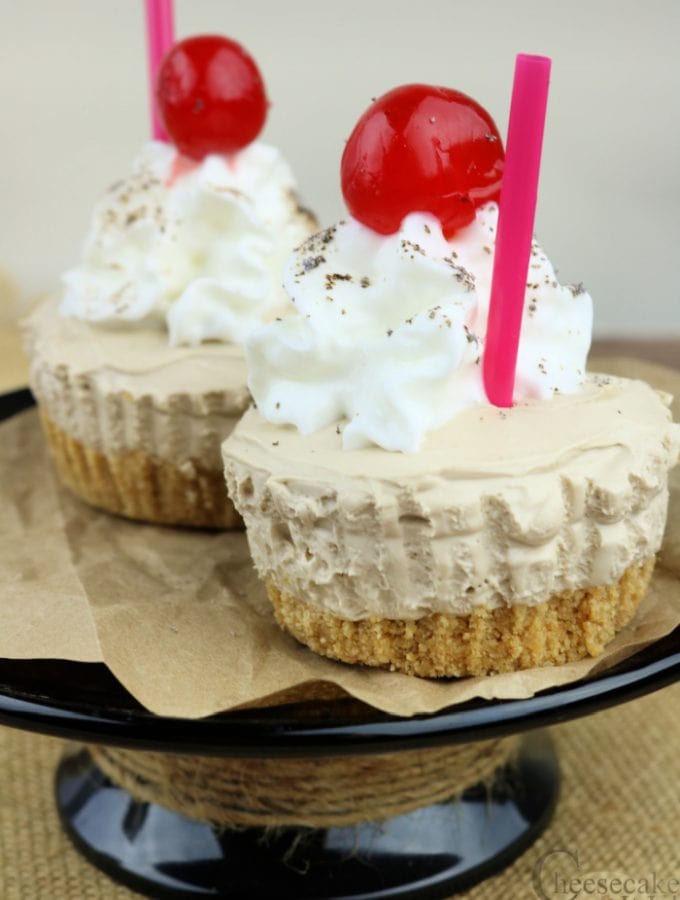 Two root beer flat mini cheesecakes with cherry on top on a black stand