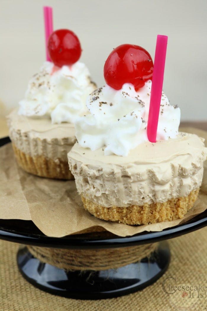 Two root beer flat mini cheesecakes with cherry on top on a black stand