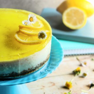 No bake lemon cheesecake on blue stand with 2 lemons in background