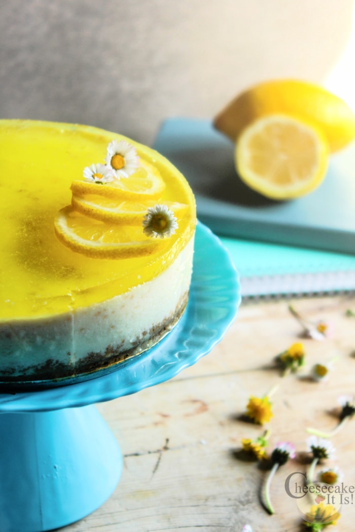 No bake lemon cheesecake on blue stand with 2 lemons in background