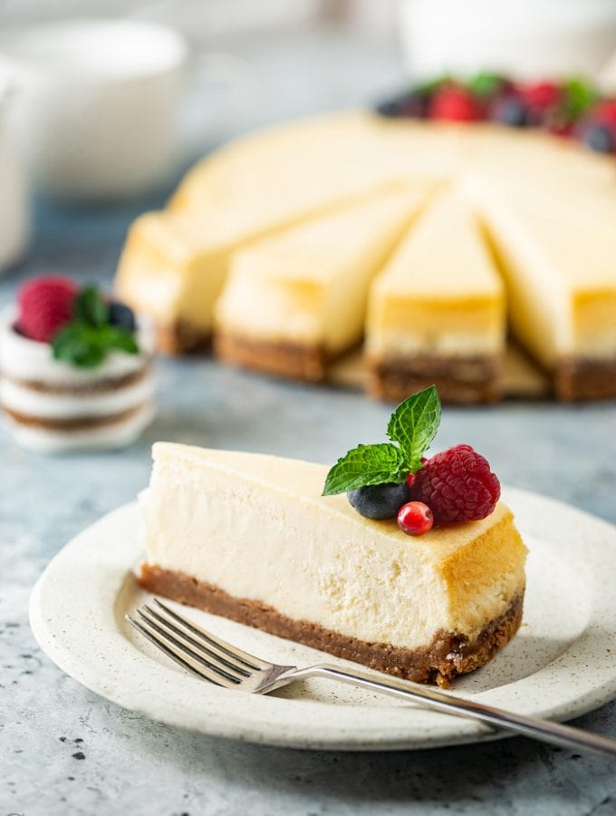 Slice of cheesecake on plate with rest of cheesecake in background