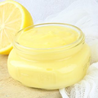 Small glass jar full of lemon curd with half lemon in background