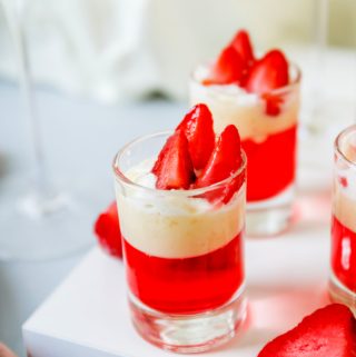 Glass shot glasses full of strawberry cheesecake pudding jello shots topped with strawberry slices