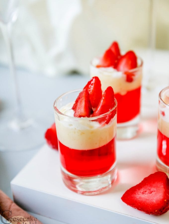 Glass shot glasses full of strawberry cheesecake pudding jello shots topped with strawberry slices