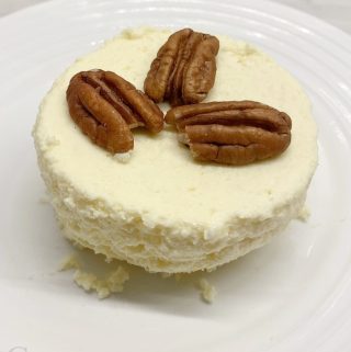 Single keto mug cheesecake on white plate with 3 pecans on top