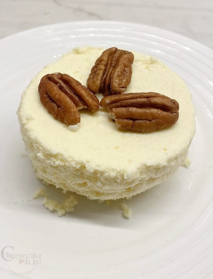 Single keto mug cheesecake on white plate with 3 pecans on top