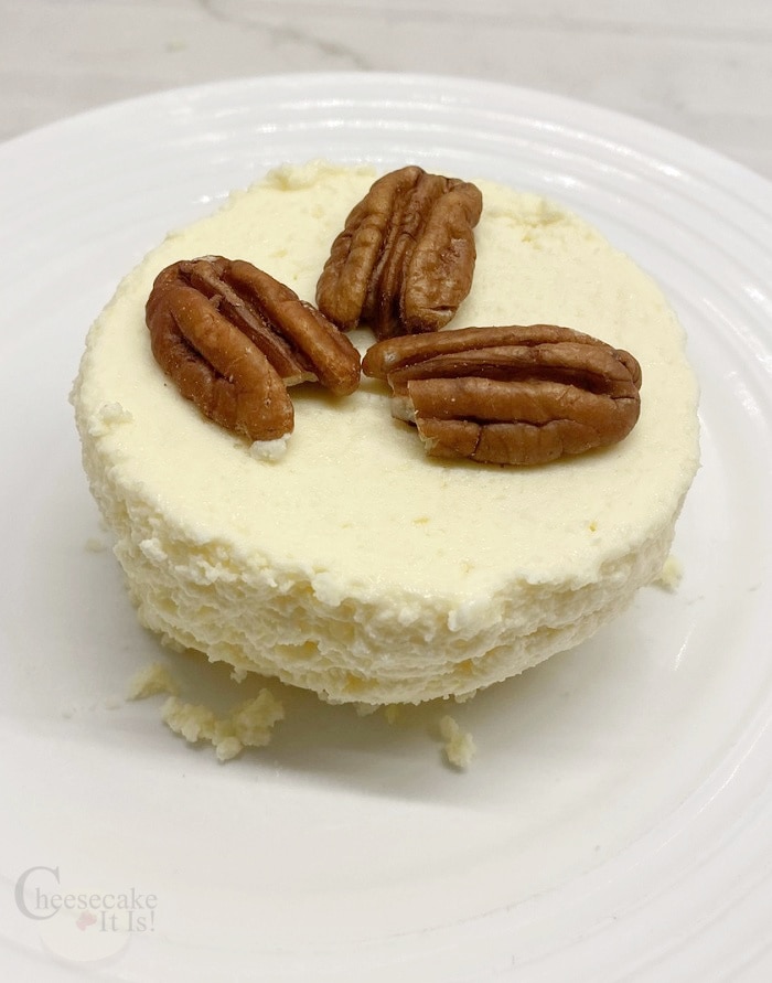 Single keto mug cheesecake on white plate with 3 pecans on top