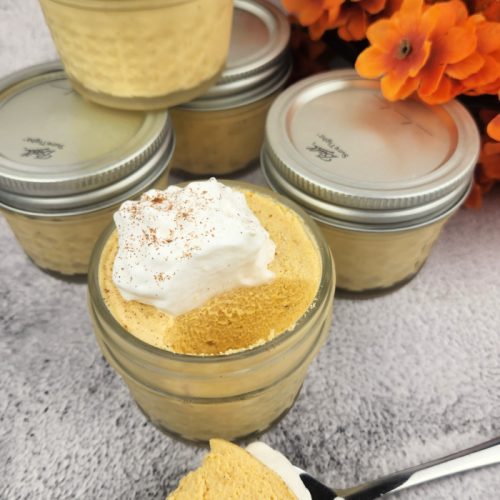 Jar of no bake keto cheesecake with a spoonful missing and laying to the side