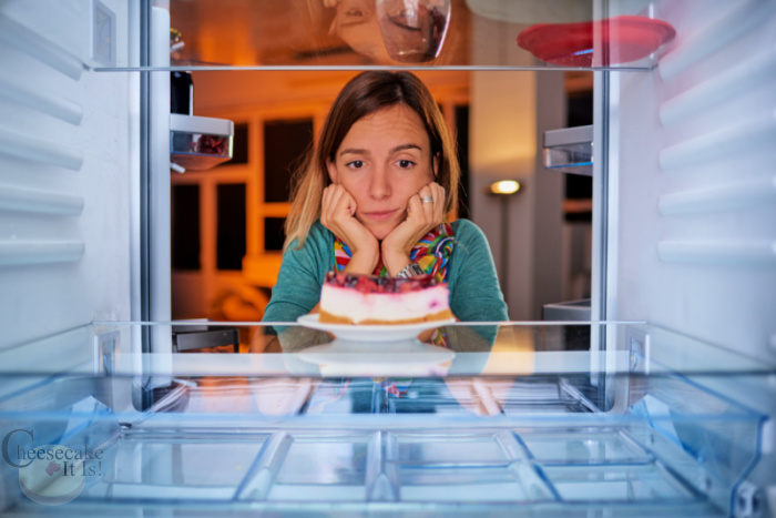 Women with hands on each side of face looking at whole cheesecake in fridge