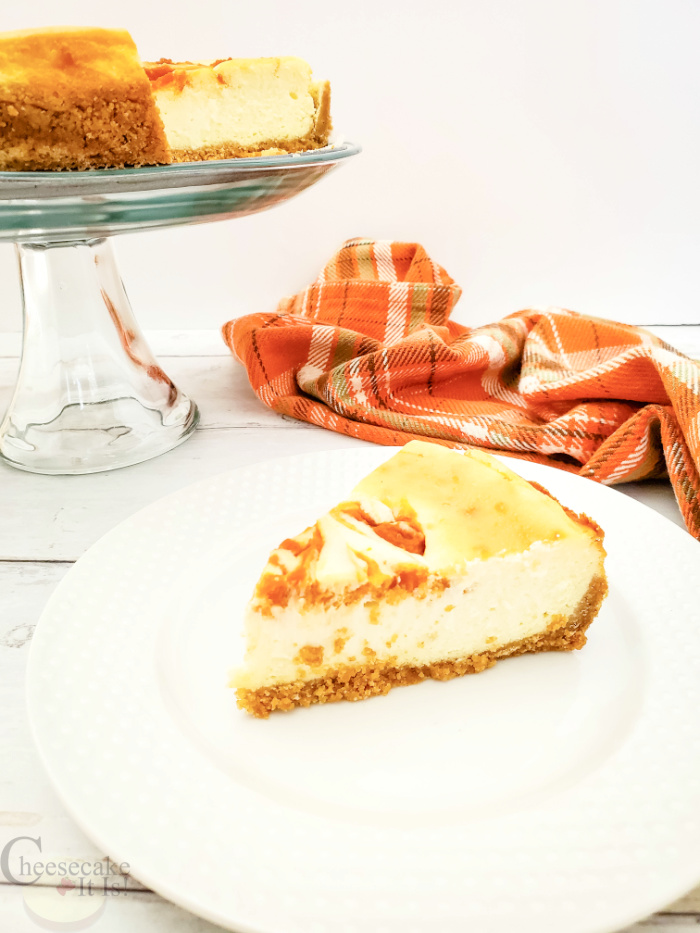 Slice of pumpkin swirl cheesecake on a white plate with rest of cheesecake in background