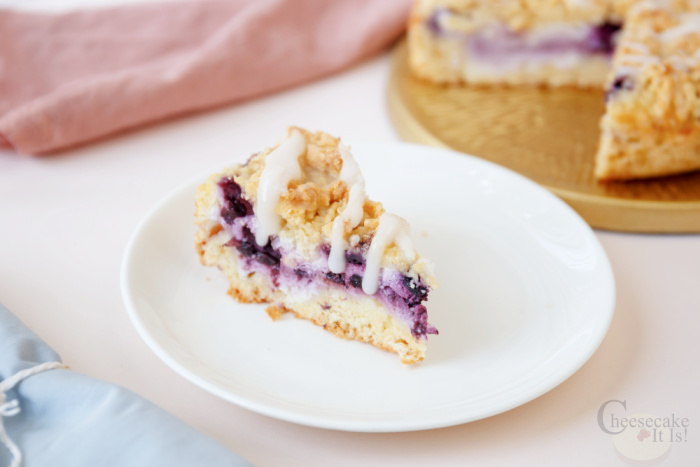 Slice of blueberry crumble cheesecake on white plate
