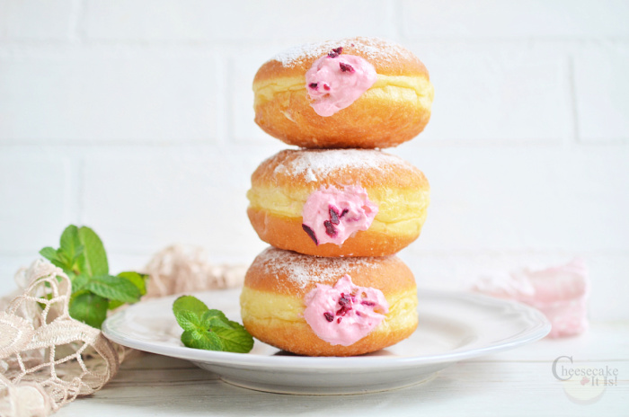 Raspberry cheesecake filled brioche donuts stacked on top of each other on white plate