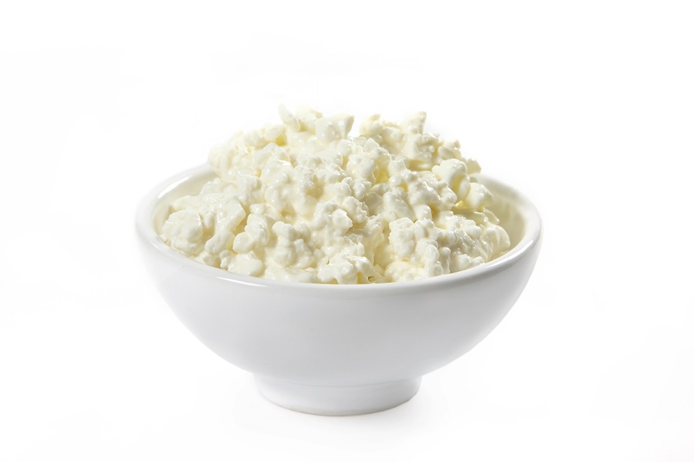 White bowl full of cottage cheese on white background