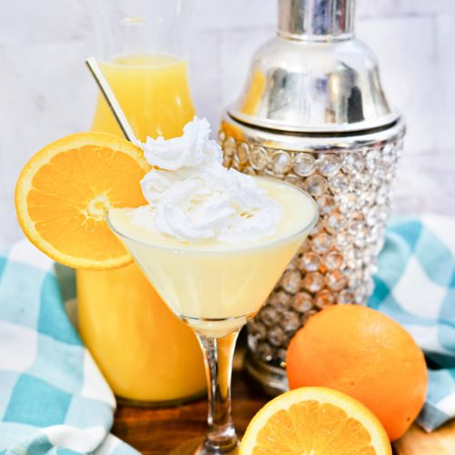 Cheesecake Orange Julius Martini in a glass topped with whipped cream and orange slice.