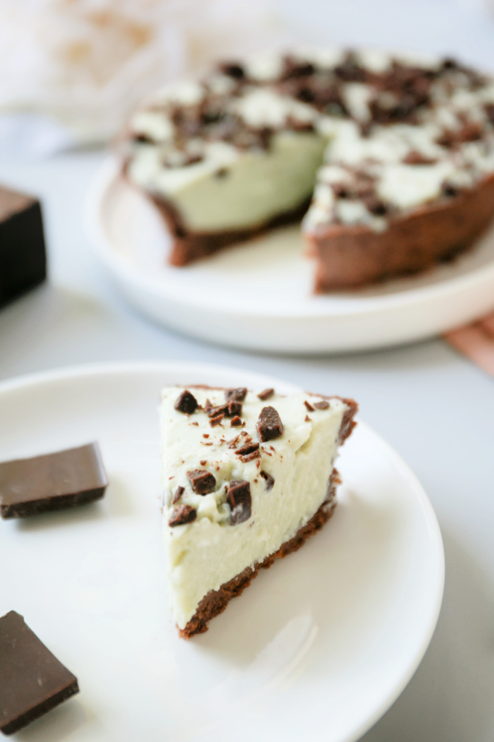 Slice of mint chocolate chip cheesecake on white plate with rest of cheesecake in background