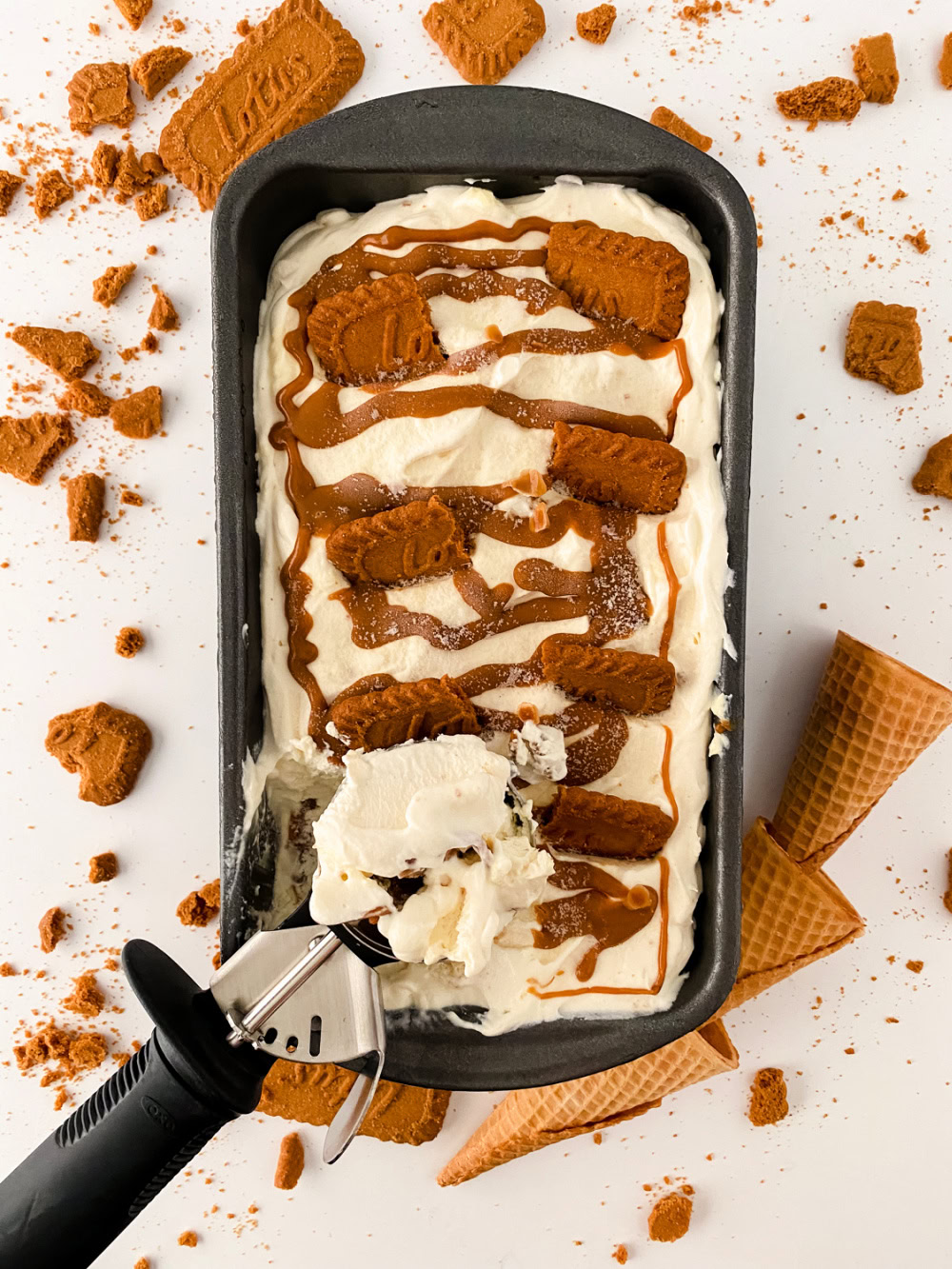 Loaf pan full of no churn biscoff cheesecake ice cream with a ice cream with a scoop digging in.