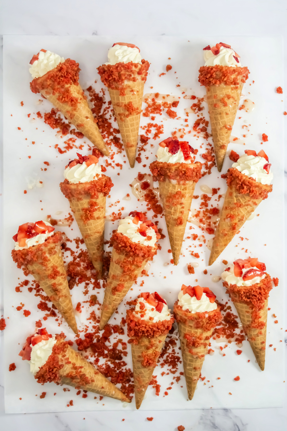 Overhead view of 12 Strawberry Crunch Cheesecake Cones On Parchment Paper
