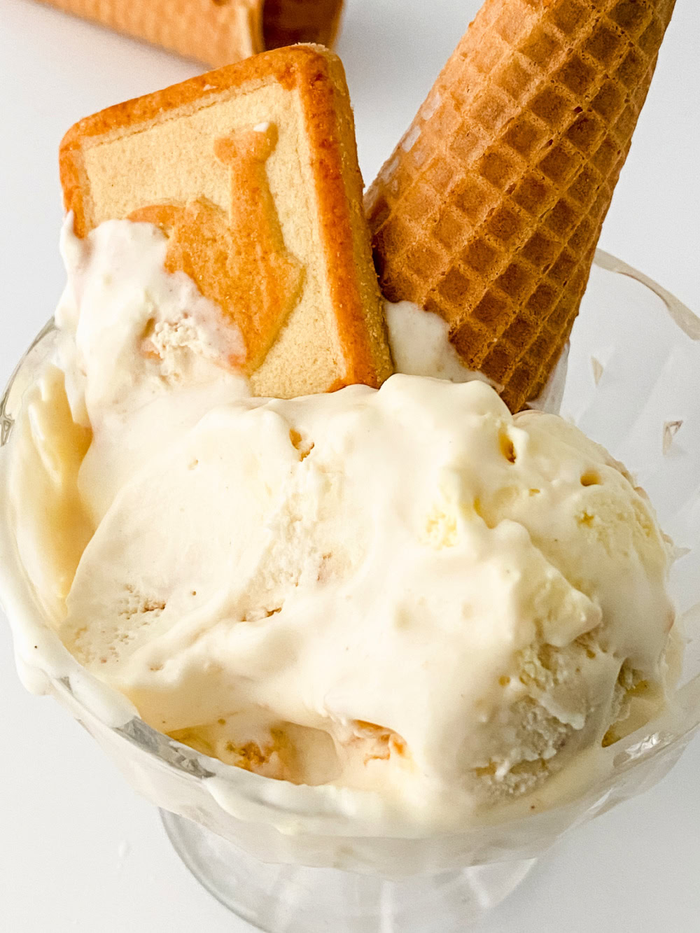 Small glass bowl full of No Churn Banana Pudding Cheesecake Ice Cream with a cone and cookie on the top 